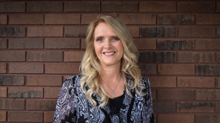 Professional woman smiling against brick wall for Huber Michaels & Company SEO image.