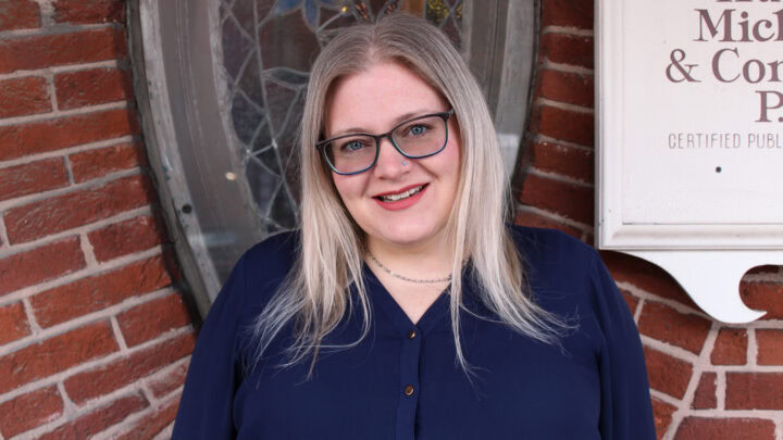 Woman smiling outside of Huber Michaels & Company law office in front of brick wall and stained glass window.