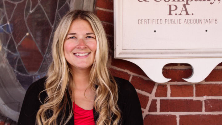 Bright smiling woman outside Huber Michaels & Company CPA office in front of brick wall.